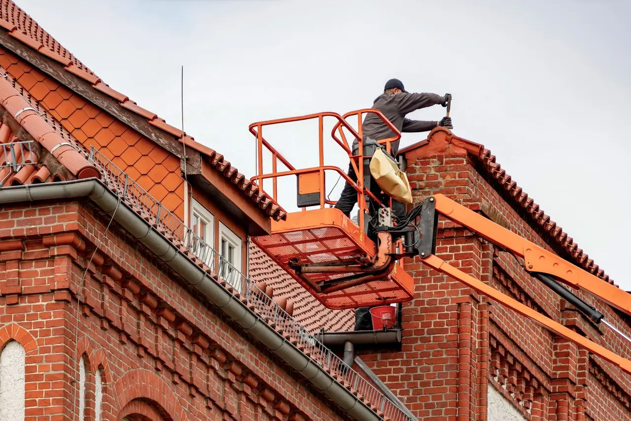Dakdekker op een hoogwerker bij een bakstenen woning