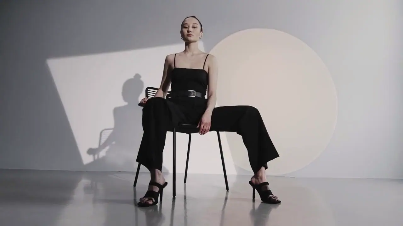 Model in Schwarz auf einem Stuhl in einem hellgrauen Raum